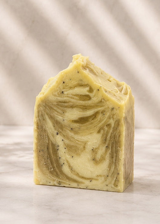 Bar of soap with green swirls on a marble surface with a plant and towel in the background