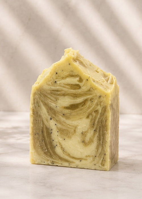 Bar of soap with green swirls on a marble surface with a plant and towel in the background